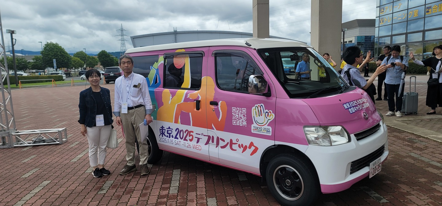 東京2025デフリンピック大会キャラバンカーの前で記念撮影する　松本 幸造理事長（全国ろうあ者大会会場 盛岡タカヤアリーナにて 6月15日(日)）